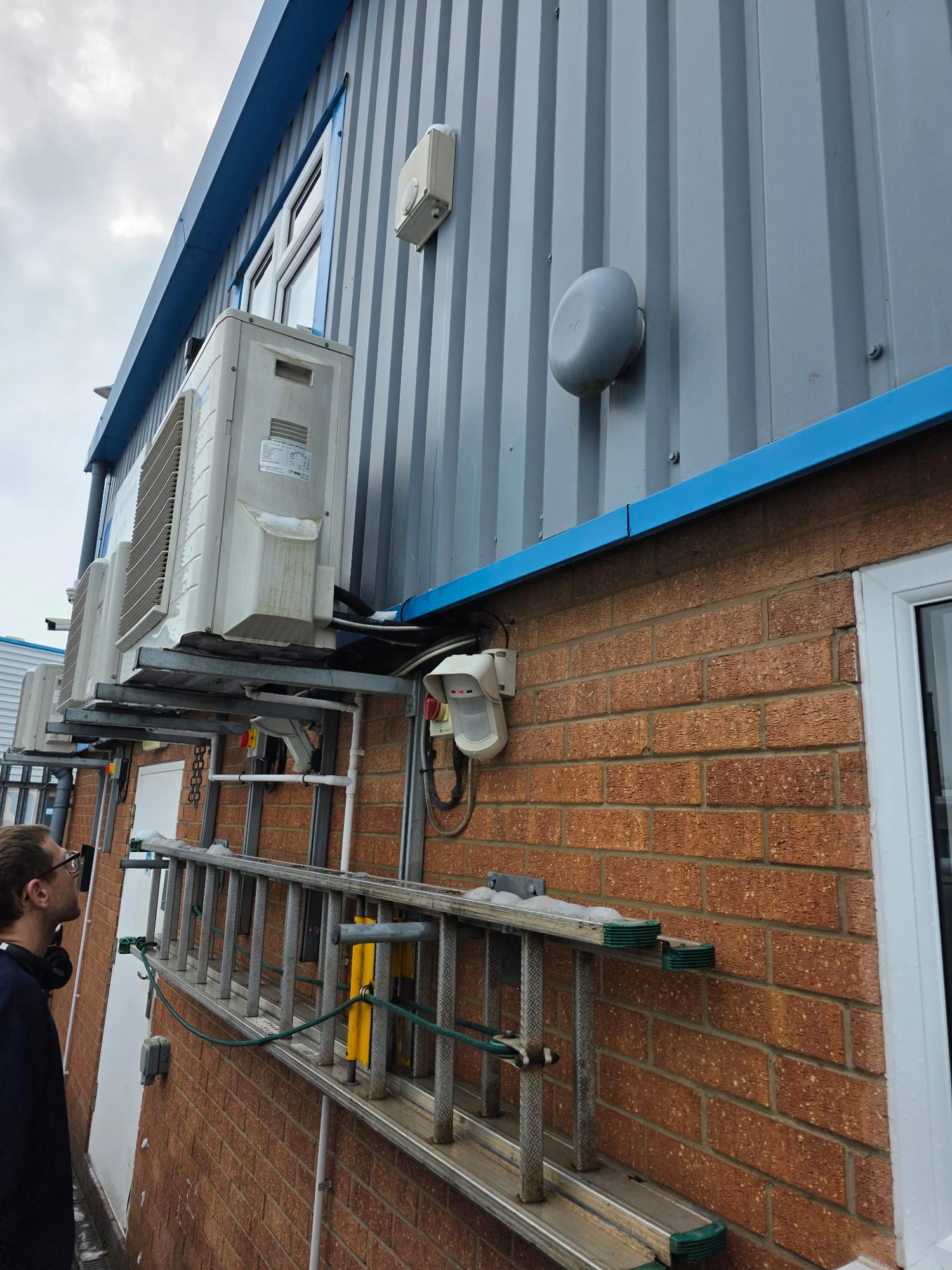 Outdoor commercial air conditioning units mounted on a building, with an OptimPRO engineer on site